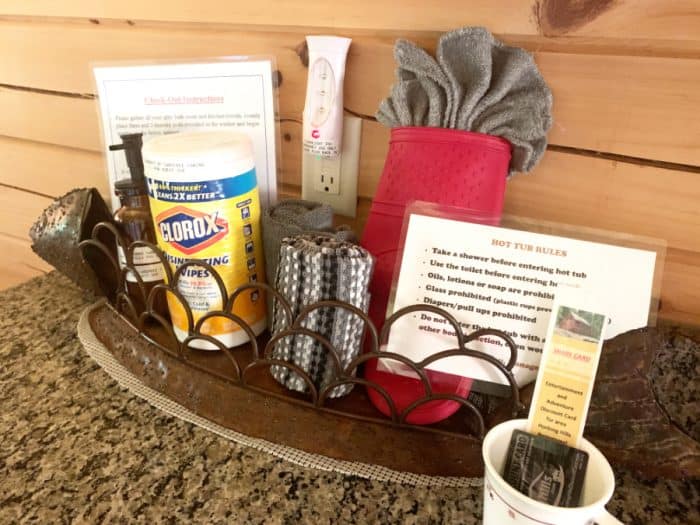 Metal basket containing a red potholder, a couple of grey kitchen towels, disinfecting wipes and 2 sets of instructions.