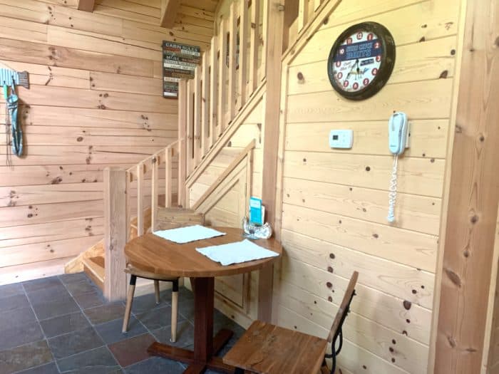Inside a cabin with light wooden walls with a staircase going up and a small kitchen table with 2 chairs