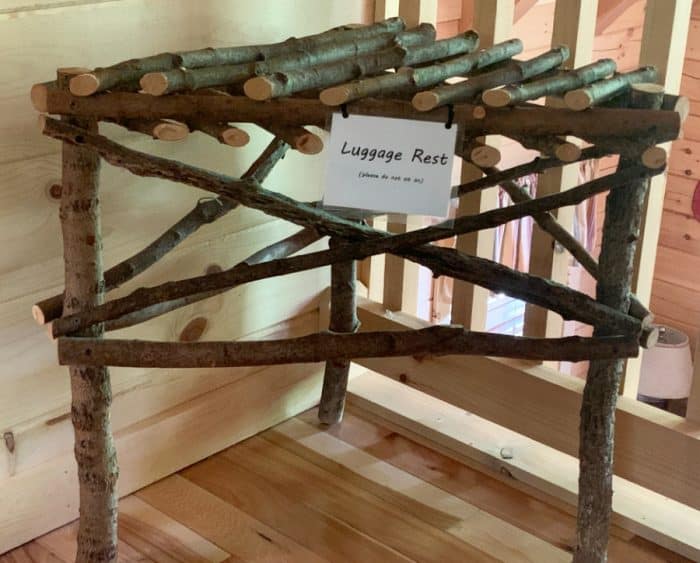 Luggage rack made from sticks tucked into a corner of a room with a white sign saying 'luggage rest'