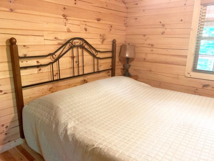 Bed with white comforter, woodend and steel headboard against a light wooden wall