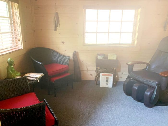 Light filled room with two brown rattan chairs on the left and a leather massage chair on the right