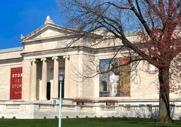 Large cream building with columns in the center and a tree on the right.