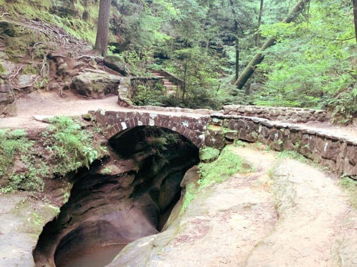 Stone bridge with a dirt trail overlooking a recessed smooth cave filled with water