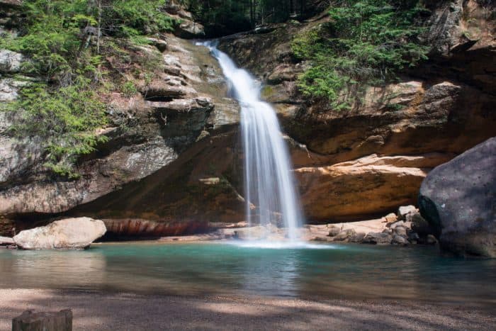 Waterfall pouring over a rock structure into a pool of water with green trees around it
