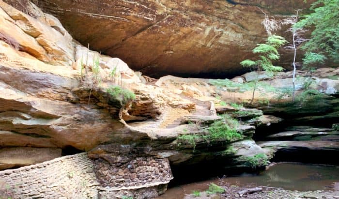 Recessed cave rock formation with a river below it and stone steps leading to it