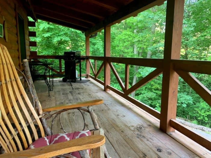 Wooden deck with brown railings and a rocking chair looking into the green forest